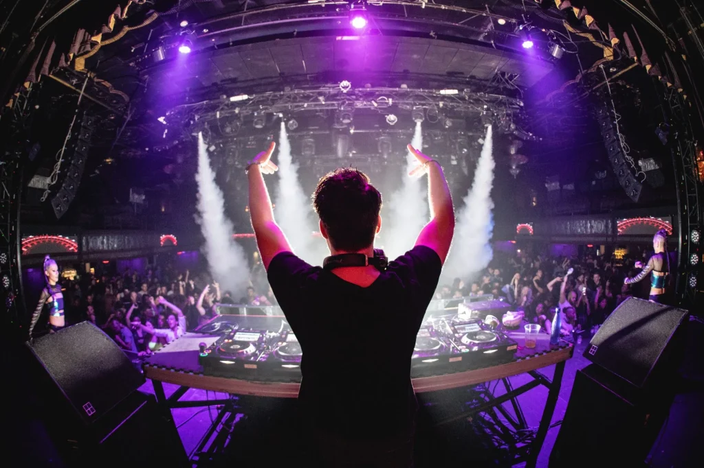 DJ in nightclub with hands up and cryo canons, shot from behind