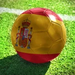football ball with the national flag of spain lies on the green field near the white line
